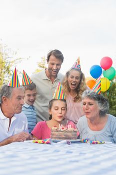 Cheerful extended family blowing out birthday candles together outside at picnic table