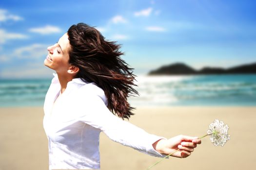 Youung woman on the beach with a flower in her hand and wind in her hair, background blured.