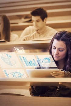 Pretty student analysing graphs on her futuristic tablet computer in lecture hall