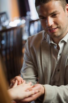 Handsome man putting on ring on his fiances finger during dinner in a classy restaurant