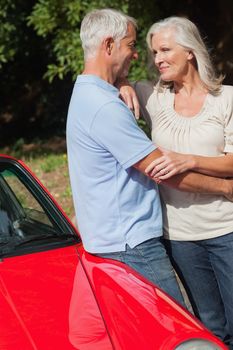 Cheerful mature couple hugging against their red cabriolet on a sunny day