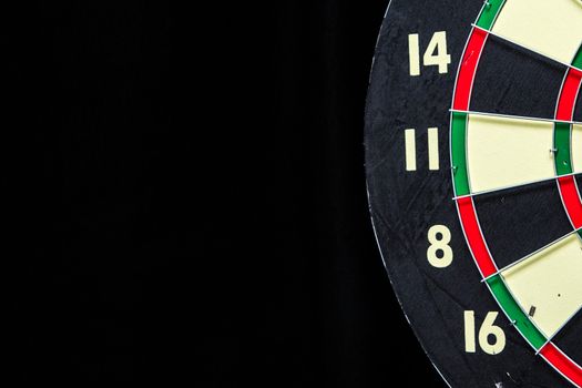 Partial red, green, black, and cream dartboard on black with copyspace on left.