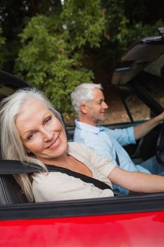 Side view of happy mature couple driving red cabriolet on sunny day