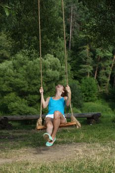 Young happy woman riding on a swing in the park