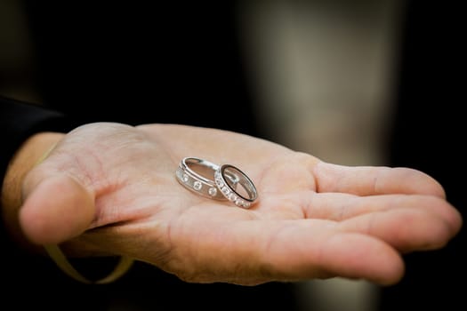 Beautiful set of wedding rings behind held by a groomsmen's hand.