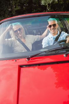 Mature couple in red cabriolet on sunny day smiling at camera 