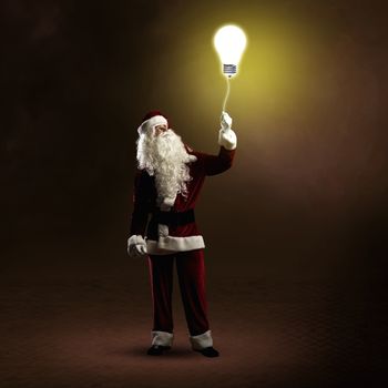 Santa Claus is holding a shining lamp on a string