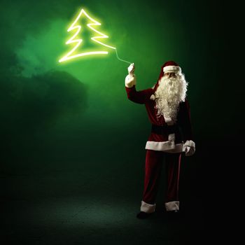 Santa Claus is holding a shining Christmas tree sign on a string