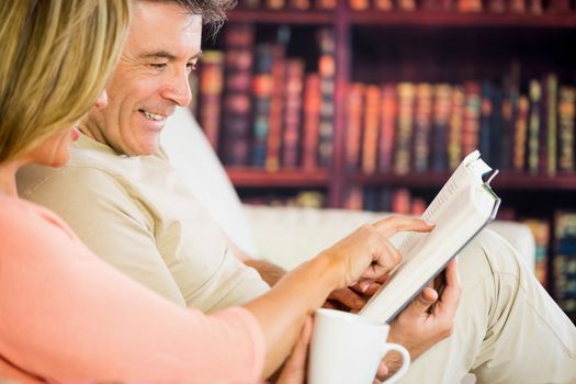 Happy mature couple reading a book in a reading room and drinking coffee