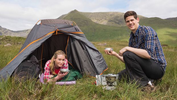 Smiling couple cooking outdoors on camping trip looking at camera