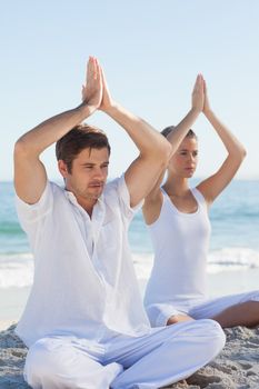 Concentrated woman and man practicing yoga at beach on a sunny day