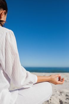 Brunette woman doing yoga at beach on a sunny day rear view