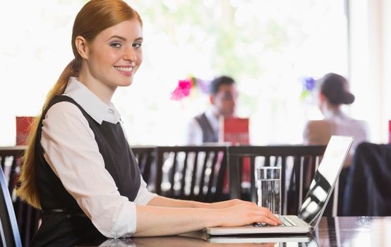 Smiling businesswoman working on laptop looking at camera in a restaurant