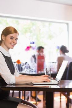 Attractive businesswoman working on laptop smiling at camera in a restaurant