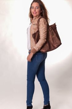 Attractive trendy young woman with long brunette hair and a handbag over her shoulder turning to look back at the camera with a lovely smile