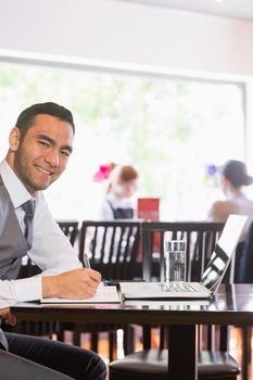 Happy businessman writing while smiling at camera in a restaurant