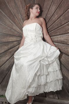 Beautiful bride in a stylish layered white wedding dress posing before a wooden panel with a radiating pattern