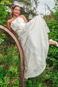 Beautiful bride in her wedding gown posing in a lush green garden with a joyful smile on her face