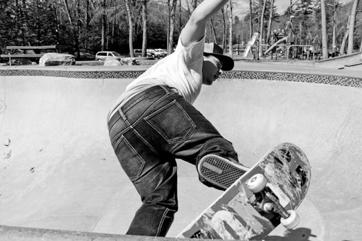 Action shot of a skateboarder skating in a concrete skateboarding bowl at the skate park. High contrast black and white.