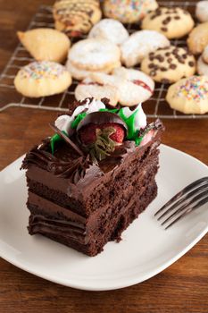 Italian cookies and a decadent slice of chocolate cake with iced flowers and chocolate covered strawberries on a plate with a fork.