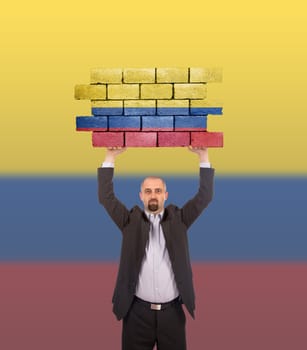 Businessman holding a large piece of a brick wall, flag of Colombia, isolated on national flag