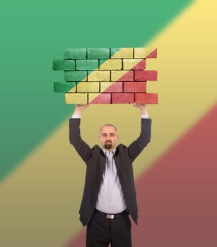 Businessman holding a large piece of a brick wall, flag of Congo, isolated on national flag