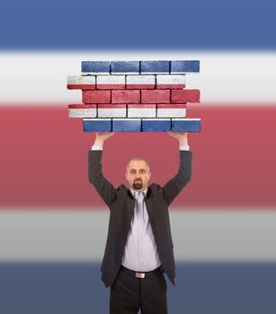 Businessman holding a large piece of a brick wall, flag of Costa Rica, isolated on national flag