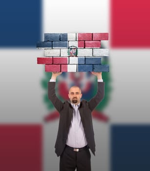 Businessman holding a large piece of a brick wall, flag of the Dominican Republic, isolated on national flag