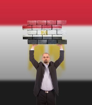 Businessman holding a large piece of a brick wall, flag of Egypt, isolated on national flag