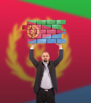 Businessman holding a large piece of a brick wall, flag of Eritrea, isolated on national flag