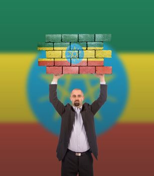 Businessman holding a large piece of a brick wall, flag of Ethiopia, isolated on national flag