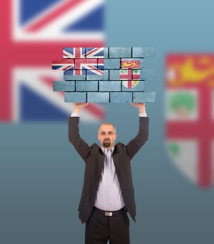 Businessman holding a large piece of a brick wall, flag of Fiji, isolated on national flag