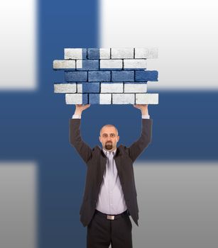 Businessman holding a large piece of a brick wall, flag of Finland, isolated on national flag