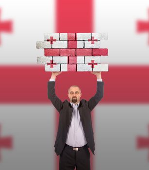 Businessman holding a large piece of a brick wall, flag of Georgia, isolated on national flag