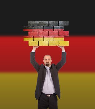 Businessman holding a large piece of a brick wall, flag of Germany, isolated on national flag