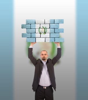 Businessman holding a large piece of a brick wall, flag of Guatemala, isolated on national flag