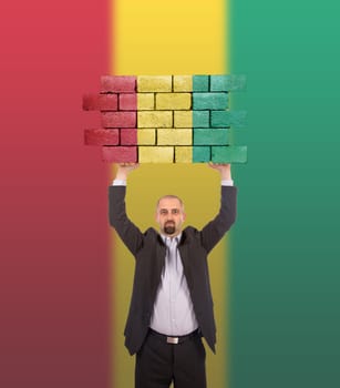Businessman holding a large piece of a brick wall, flag of Guinea, isolated on national flag