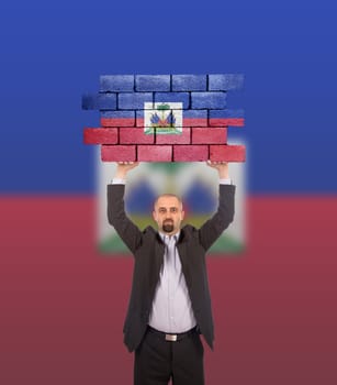 Businessman holding a large piece of a brick wall, flag of Haiti, isolated on national flag