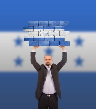 Businessman holding a large piece of a brick wall, flag of Honduras, isolated on national flag