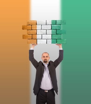 Businessman holding a large piece of a brick wall, flag of Ivory Coast, isolated on national flag