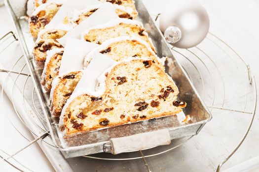 christmas stollen cake on a silver metal tray on a cooling grid with a silver christmas ball