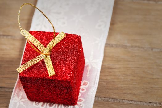 closeup of a red tiny glitter christmas present on a golden ribbon on wooden background