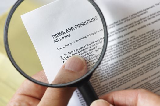 hands holding magnifying glass reading terms and conditions of loan agreement