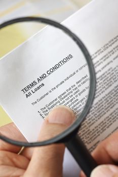 hands holding magnifying glass reading terms and conditions of loan agreement