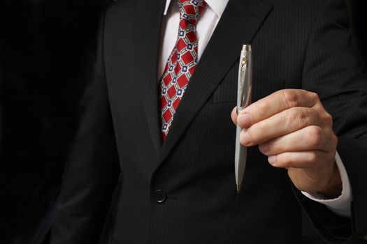 businessman in suit holding out pen towards camera