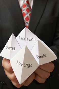 Business man holding paper origami fortune teller with savings,bonds,shares and pensions written on it