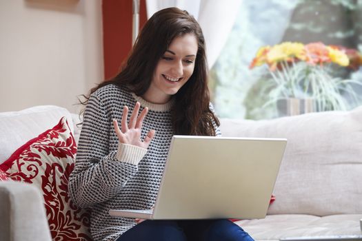 teenage girl waving at laptop while using webcam at home