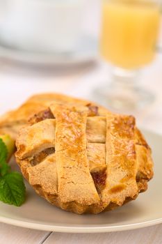 Small round apple pie with lattice crust with mint leaf on a plate, hot apple punch in the back (Selective Focus, Focus one third into the pie) 