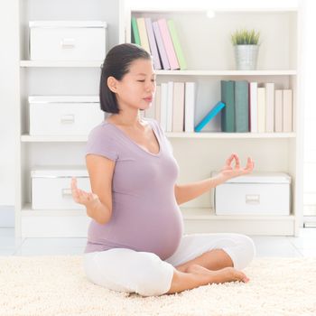 Pregnancy yoga meditation. Full length healthy 8 months pregnant calm Asian woman meditating or doing yoga exercise at home. Relaxation yoga pose.