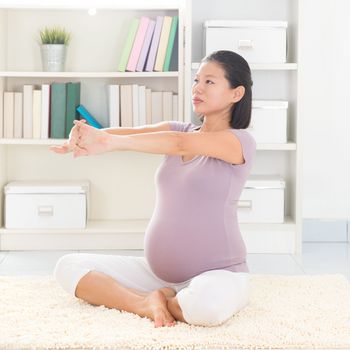 Pregnancy yoga meditation. Full length healthy 8 months pregnant calm Asian woman meditating or doing yoga exercise at home. Relaxation yoga arms stretching pose.